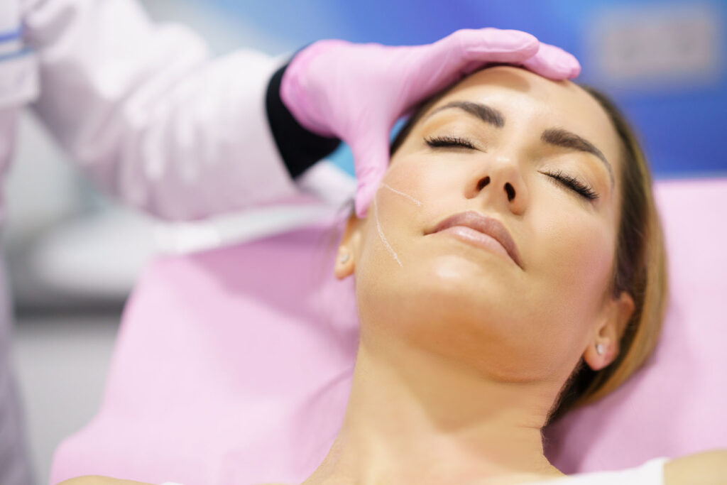 person lying on a treatment chair with eyes closed as a practitioner in pink gloves touches their forehead