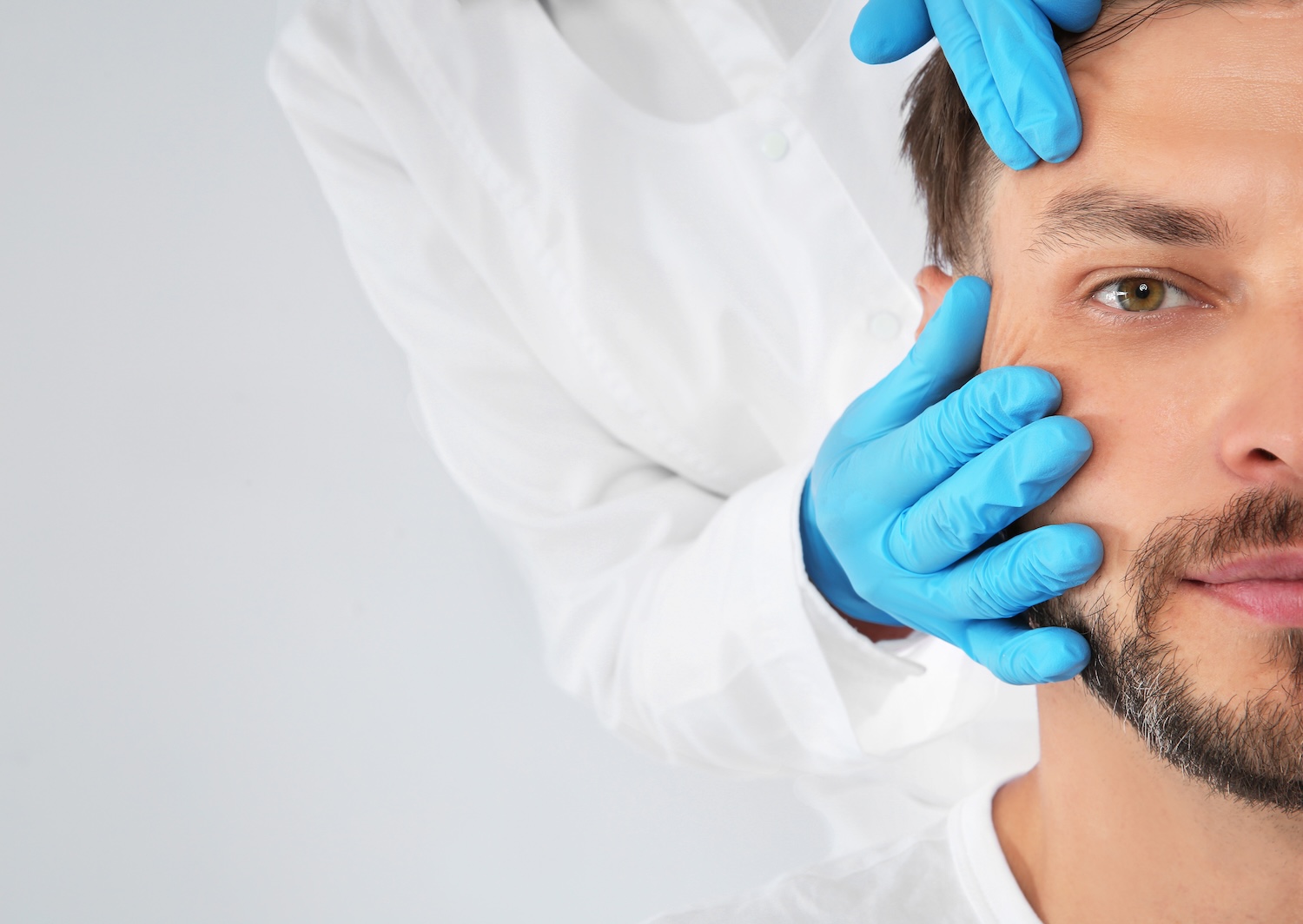 Close-up of a man’s face as a practitioner wearing blue gloves gently holds his cheek and forehead.