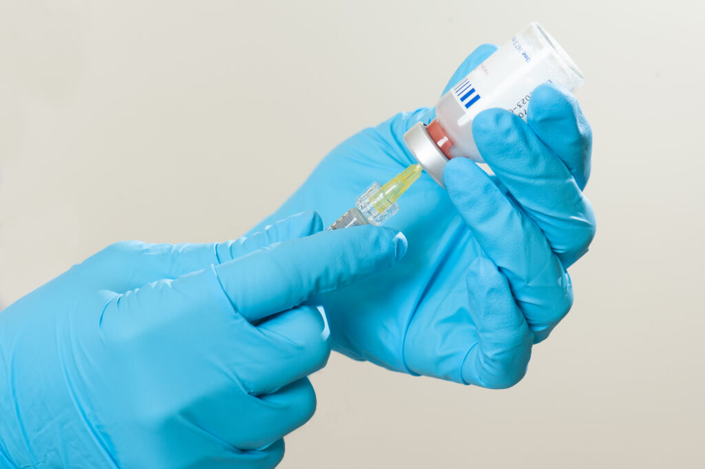 Gloved hands drawing liquid from vial into syringe