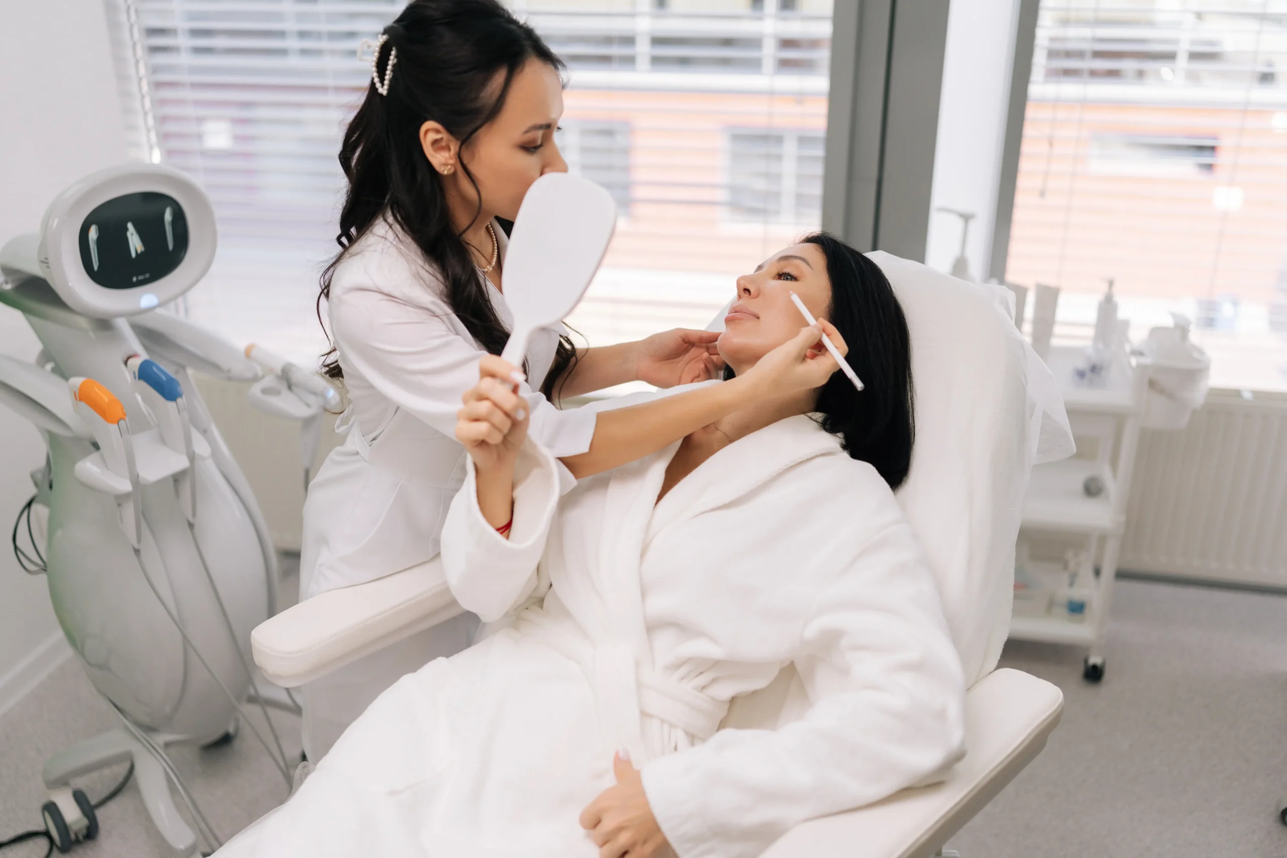 Practitioner examining woman’s face with mirror during consultation in clinic
