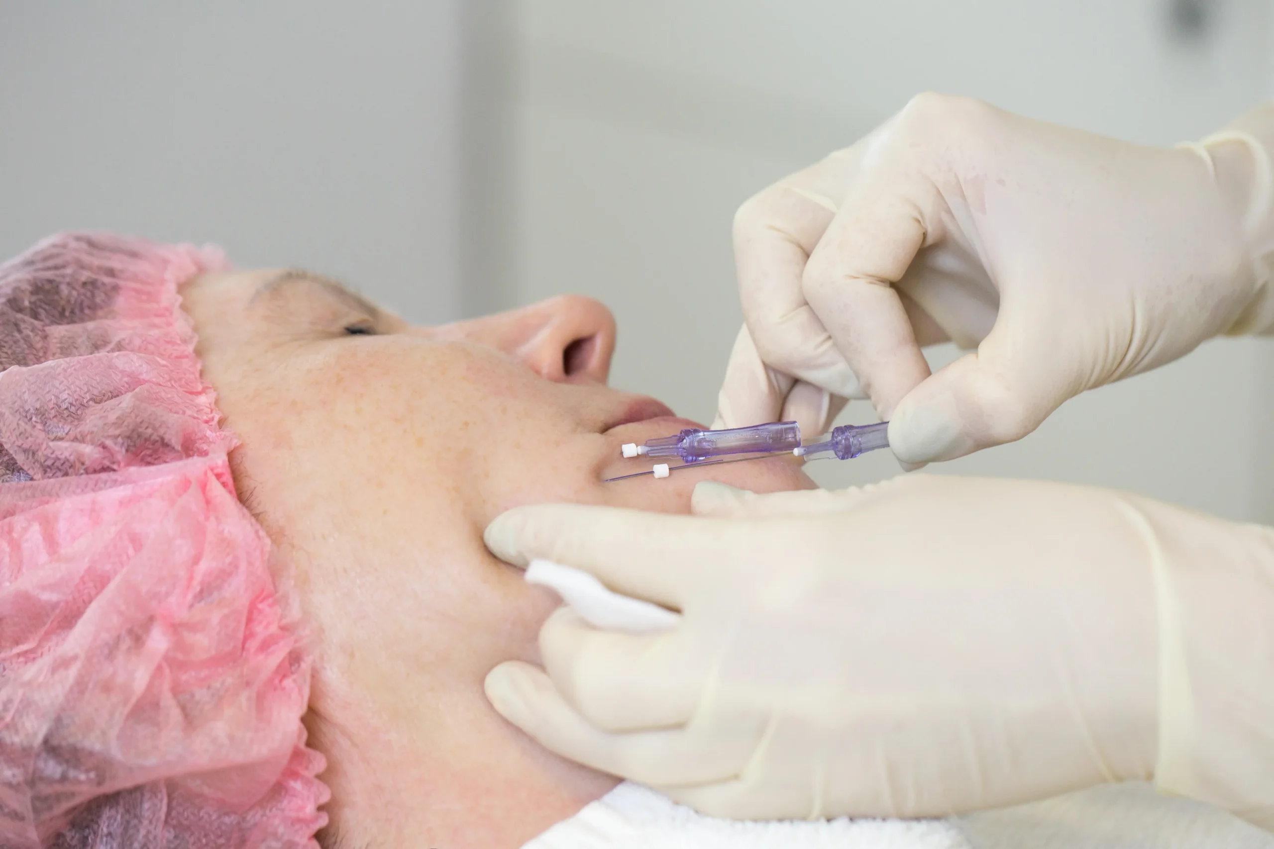 Practitioner administering injection to woman’s cheek during facial treatment