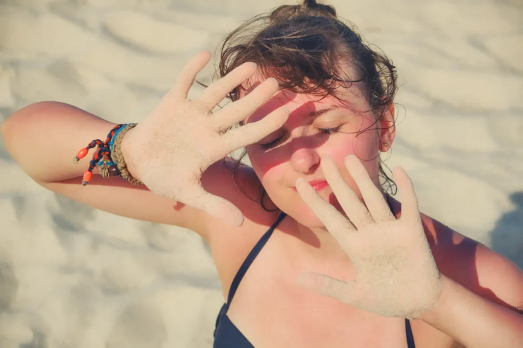 Woman on a beach covering her sunburned face with sandy hands
