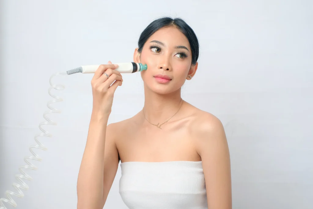 Woman holding a handheld skincare device against her cheek while looking to the side