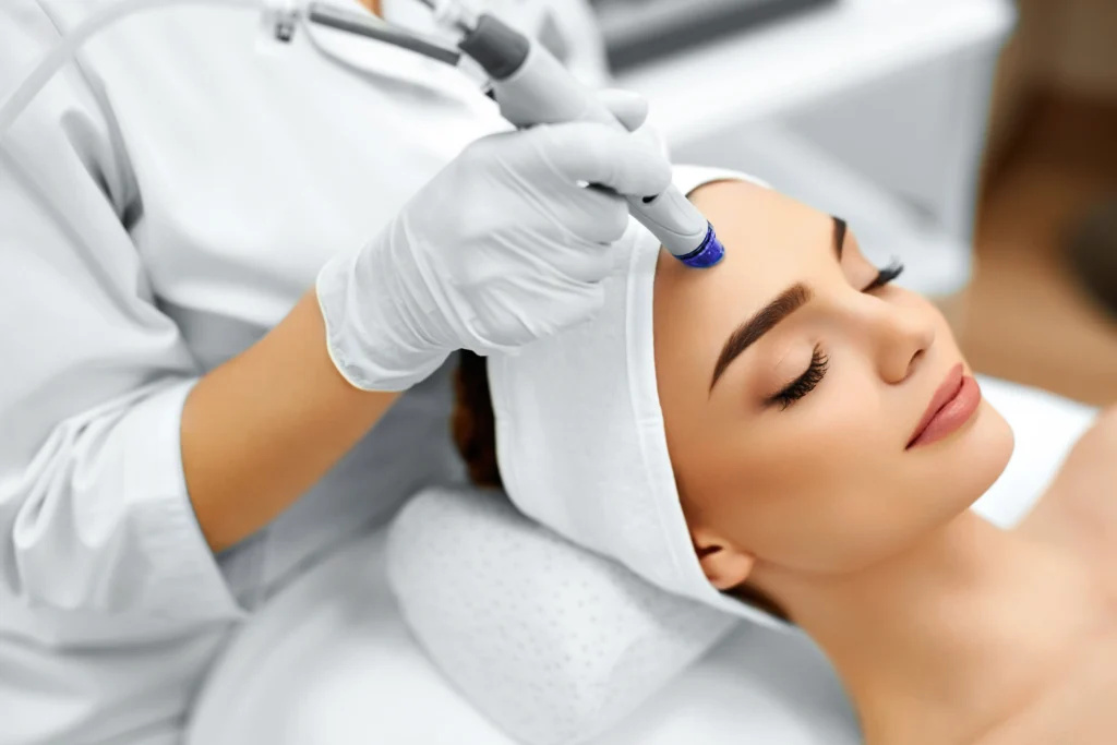 Practitioner using a handheld skin treatment device on a woman's forehead during a facial procedure