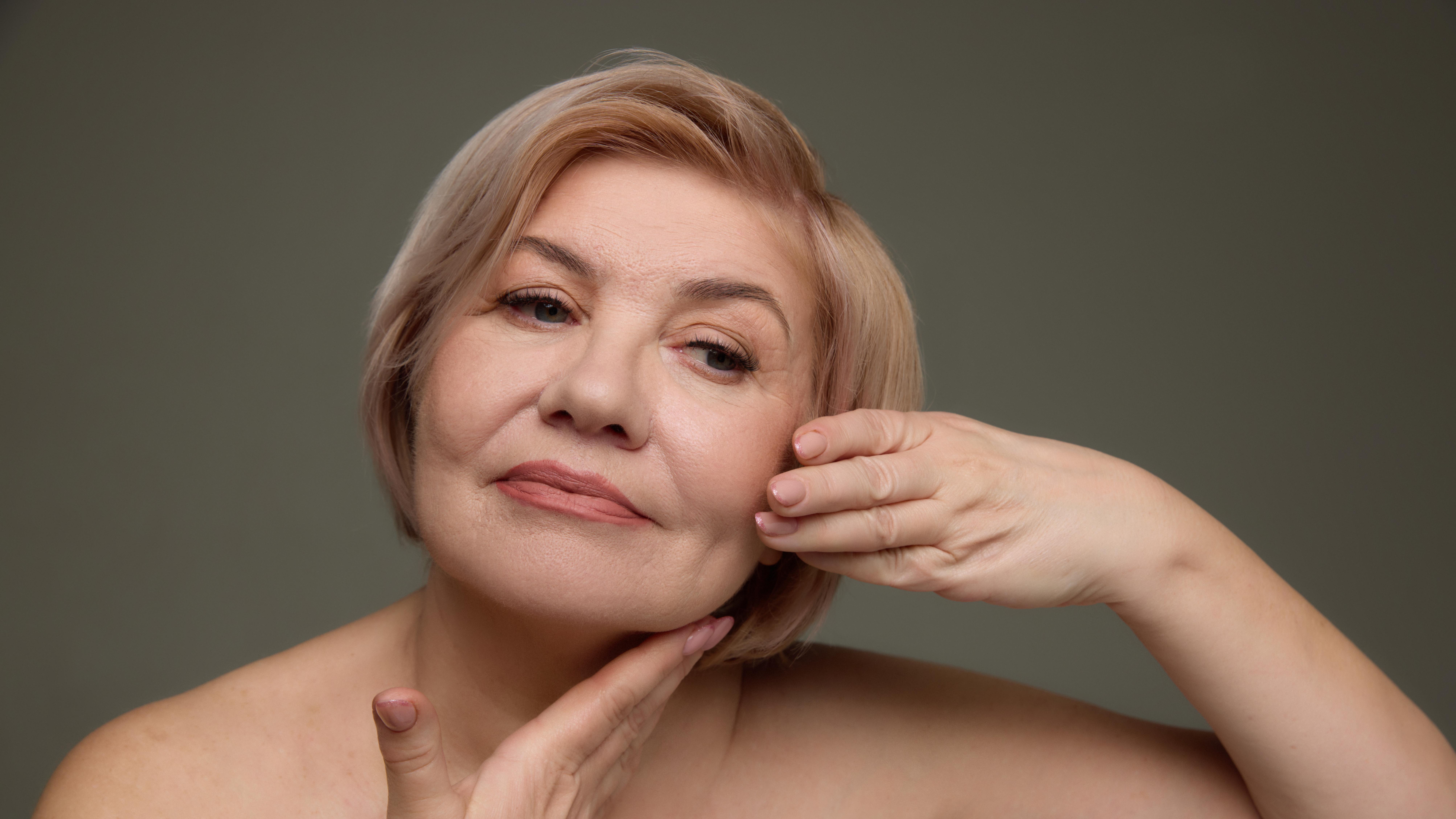 Mature woman touching her jawline and cheek while looking forward