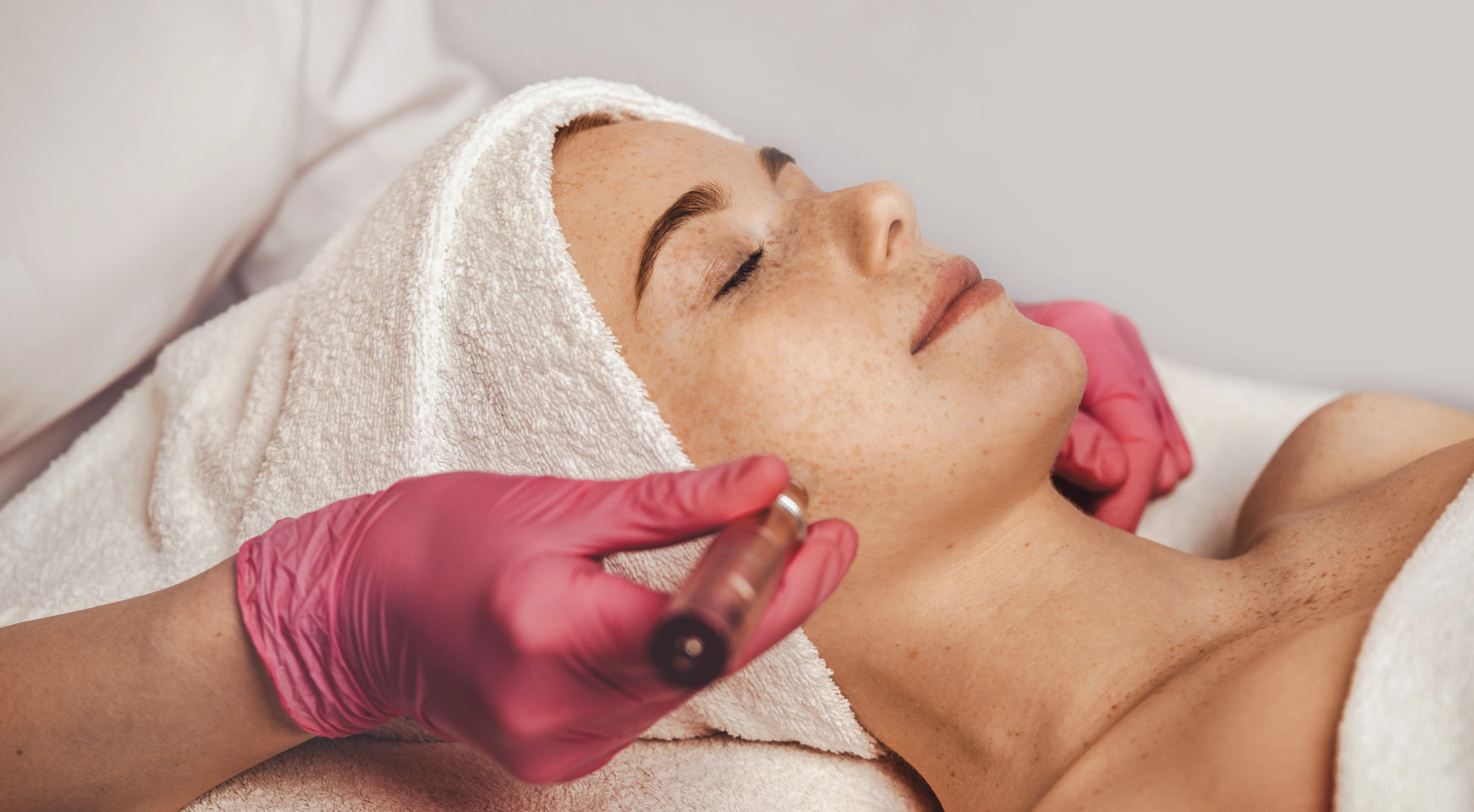 Practitioner using a handheld device on a woman's cheek during a facial treatment
