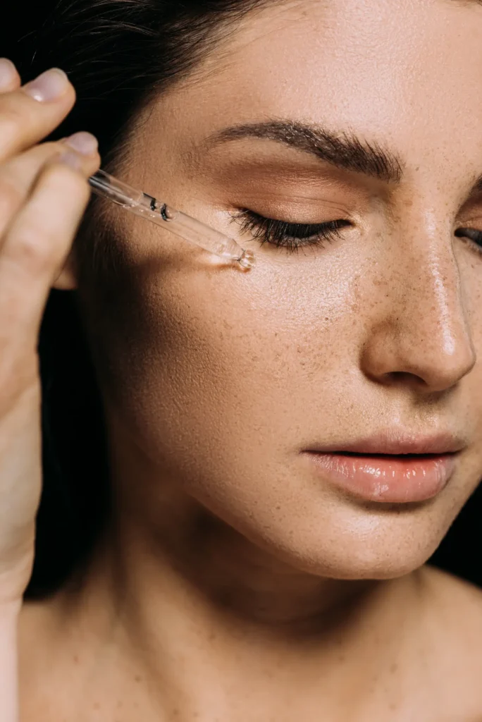 Close-up of a woman with eyes closed and a glass dropper held beneath one eye.