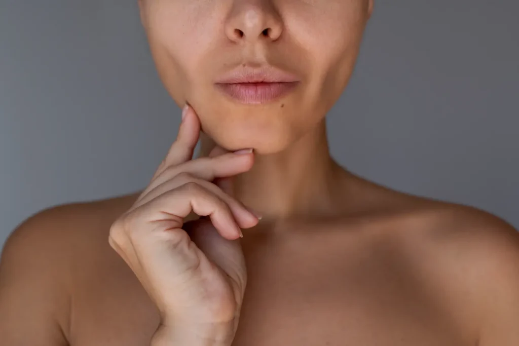 Close-up of a woman touching the side of her lower jaw with her fingertips against a gray background.