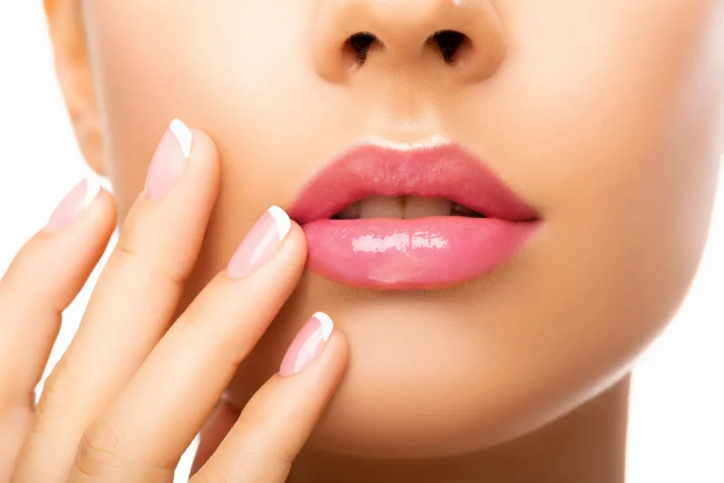 Close-up of glossy pink lips with manicured fingers resting beside the mouth.
